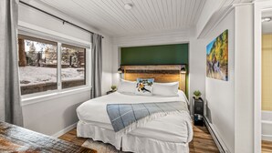 Ein Schlafzimmer mit einem großen Bett, einem Fenster mit Blick auf einen verschneiten Garten und einer grünen Akzentwand, sowie einem Bild an der Wand.