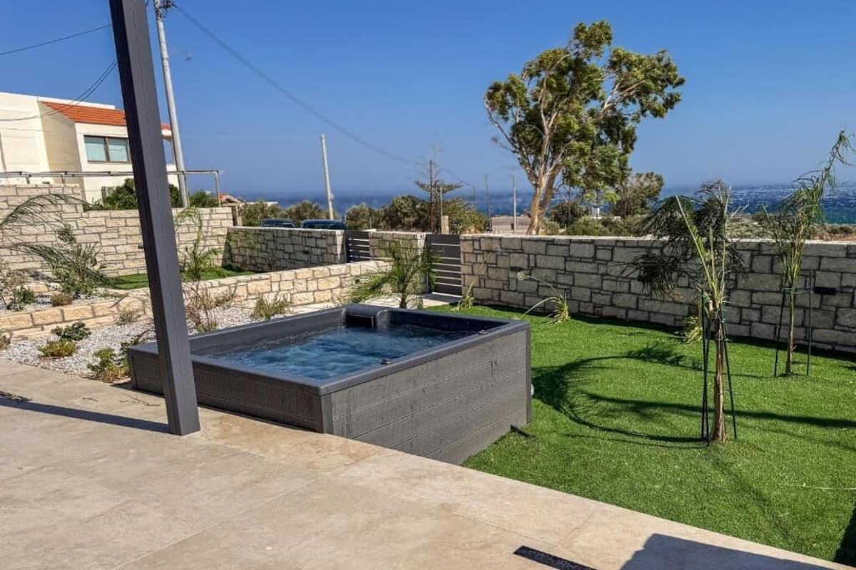 A modern outdoor hot tub area with a stone wall and a view of the sea.