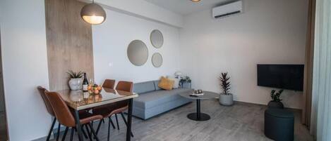 A modern living room with a dining area, a grey sofa, a round coffee table, and a TV mounted on the wall.