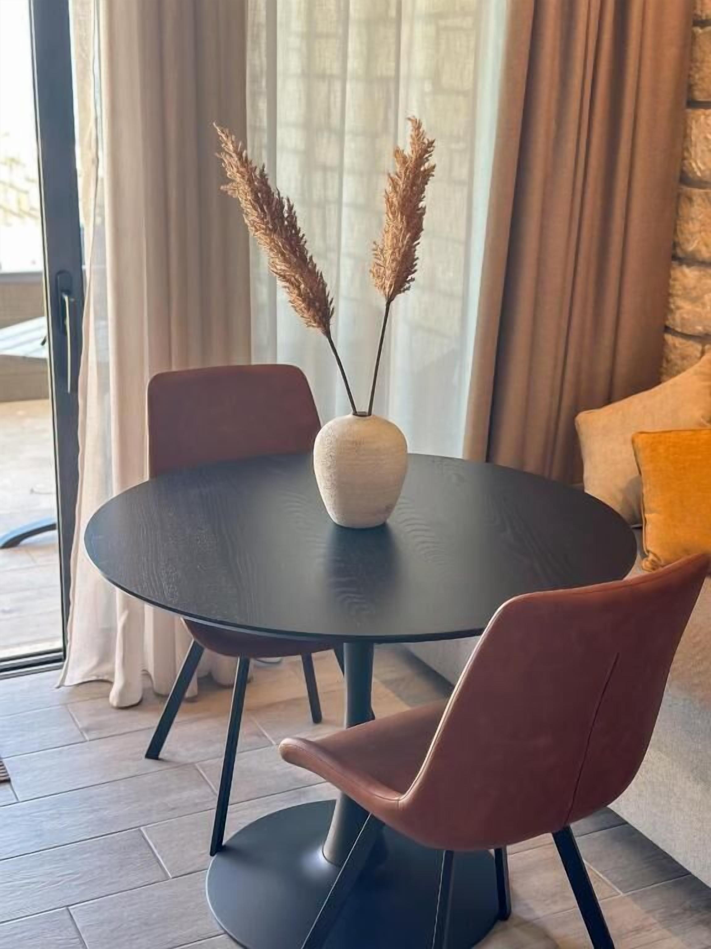 Une table de salle à manger ronde, sur laquelle se trouve un vase blanc et des plumes d’herbe des pampas, entourée de deux chaises.