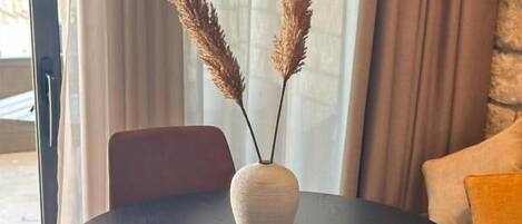 Une table de salle à manger ronde, sur laquelle se trouve un vase blanc et des plumes d’herbe des pampas, entourée de deux chaises.