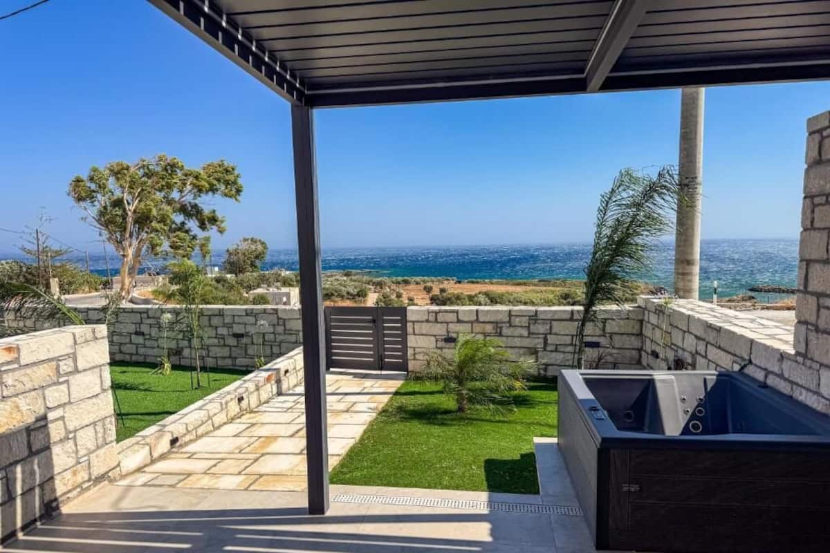 A covered outdoor area with a view of the sea, stone walls, and a small lawn.