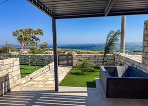 Un espacio al aire libre techado con vistas al mar, paredes de piedra y un pequeño césped.