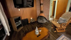 Un salon avec une cheminée, un téléviseur fixé au mur et un plancher en bois.