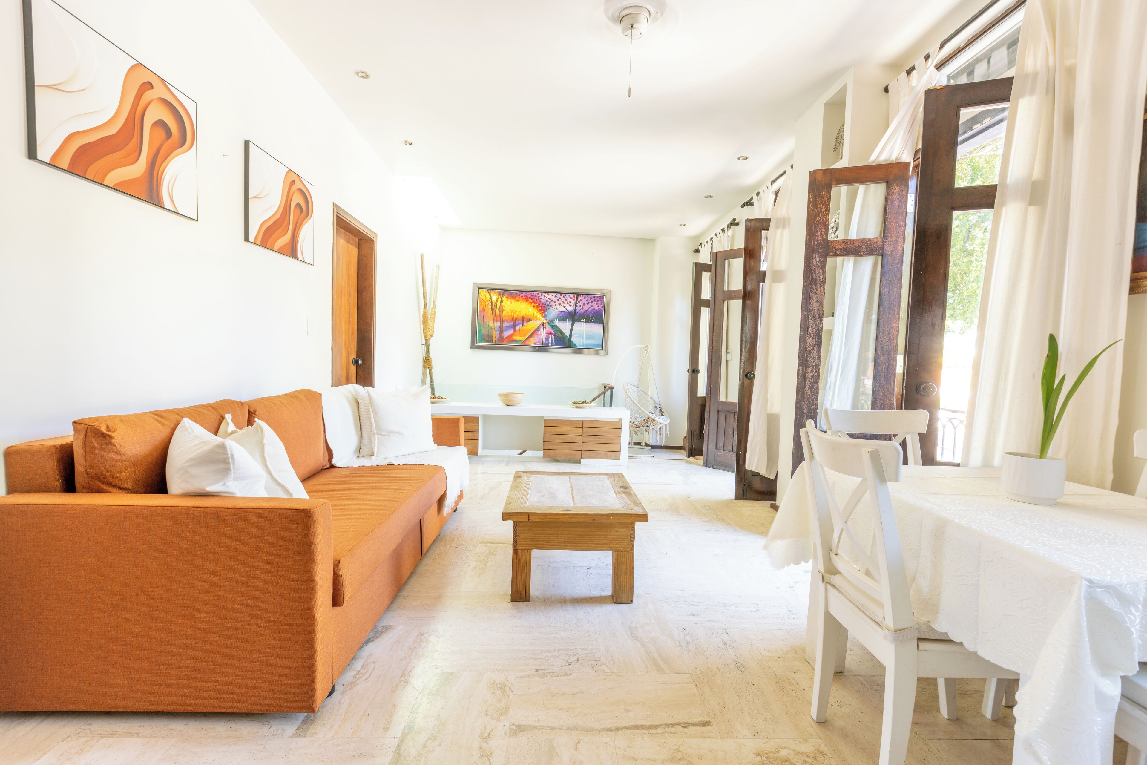 Un salon spacieux comprenant un canapé, une table basse et une table à manger. Les murs sont ornés de tableaux et il y a une fenêtre avec des rideaux.