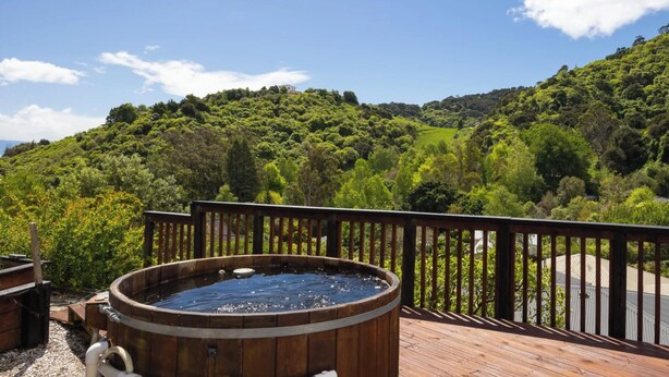 A wooden deck with a hot tub overlooking a lush green landscape. - Tranquil Nelson Escape: Birdsong, Hot Tub, Parking. One bedroom, living room. (Nelson)