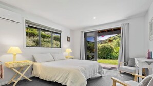 A bedroom with a bed, two bedside lamps, a chair, and a view of a garden through a sliding door. - Tranquil Nelson Escape: Birdsong, Hot Tub, Parking. One bedroom, living room. (Nelson)