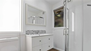 A modern bathroom with a white vanity, a glass shower enclosure, and a window with a view. - Tranquil Nelson Escape: Birdsong, Hot Tub, Parking. One bedroom, living room. (Nelson)