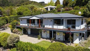 A modern two-story house with a balcony, surrounded by lush greenery and hills. - Tranquil Nelson Escape: Birdsong, Hot Tub, Parking. One bedroom, living room. (Nelson)