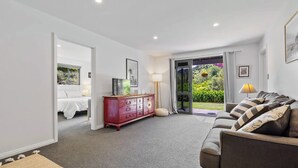 A modern living room with a sofa, a red dresser, and a bed in the adjacent room. - Tranquil Nelson Escape: Birdsong, Hot Tub, Parking. One bedroom, living room. (Nelson)