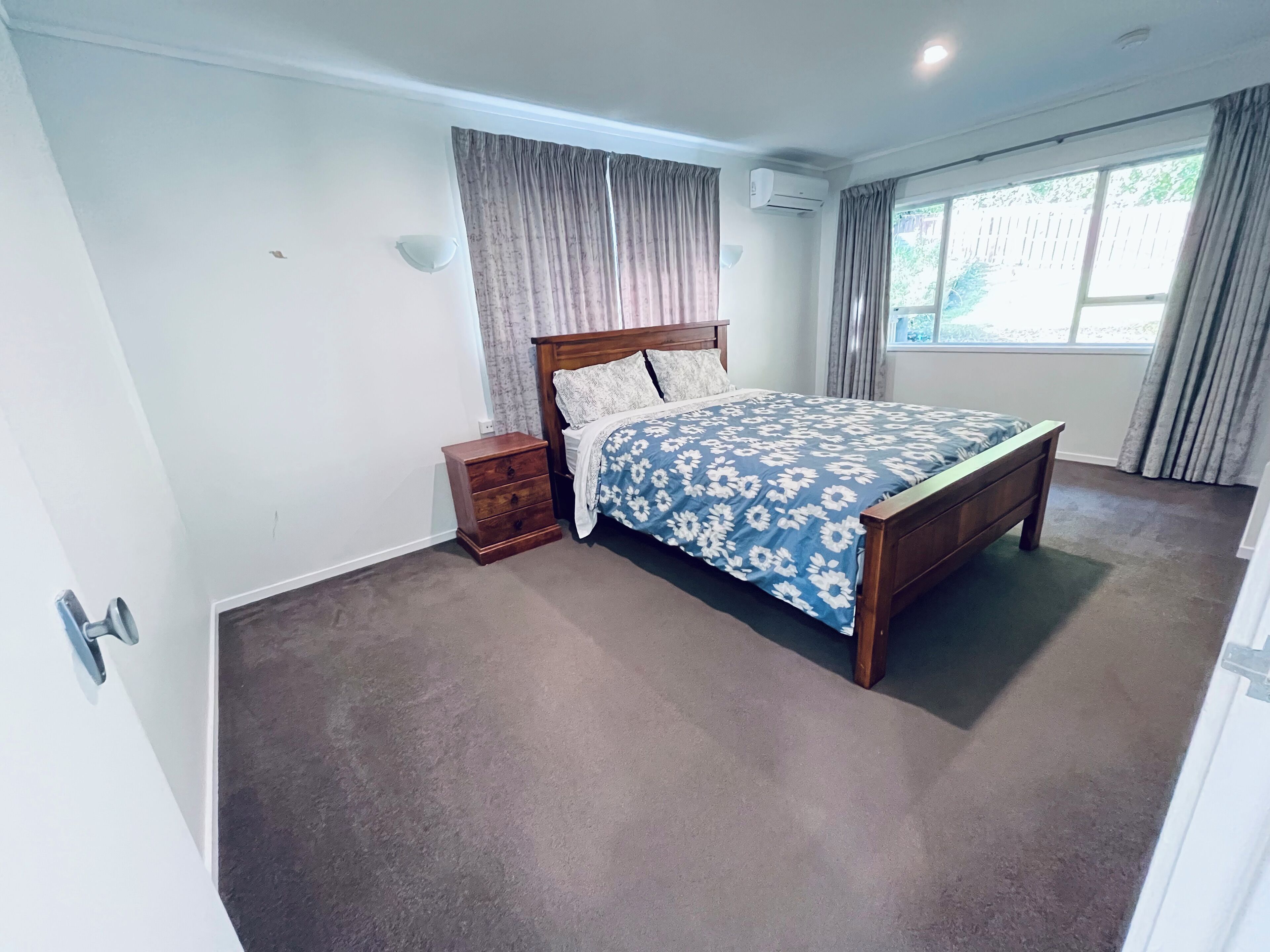 Una camera da letto con un letto, un comodino, una finestra con tende e un condizionatore.