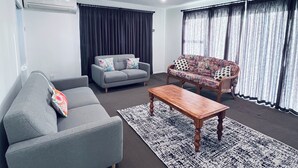 A modern living room with a grey sofa, a patterned armchair, a wooden coffee table, and a patterned rug. - Holiday Home In Red Hill Papakura Auckland With Beautiful Views (Papakura)