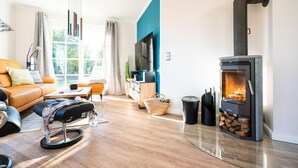 Un salon moderne avec un canapé, un pouf, une télévision et un poêle à bois.