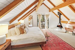 Ein Schlafzimmer mit einem großen Bett, Holzboden, Kamin und Blick ins Freie.