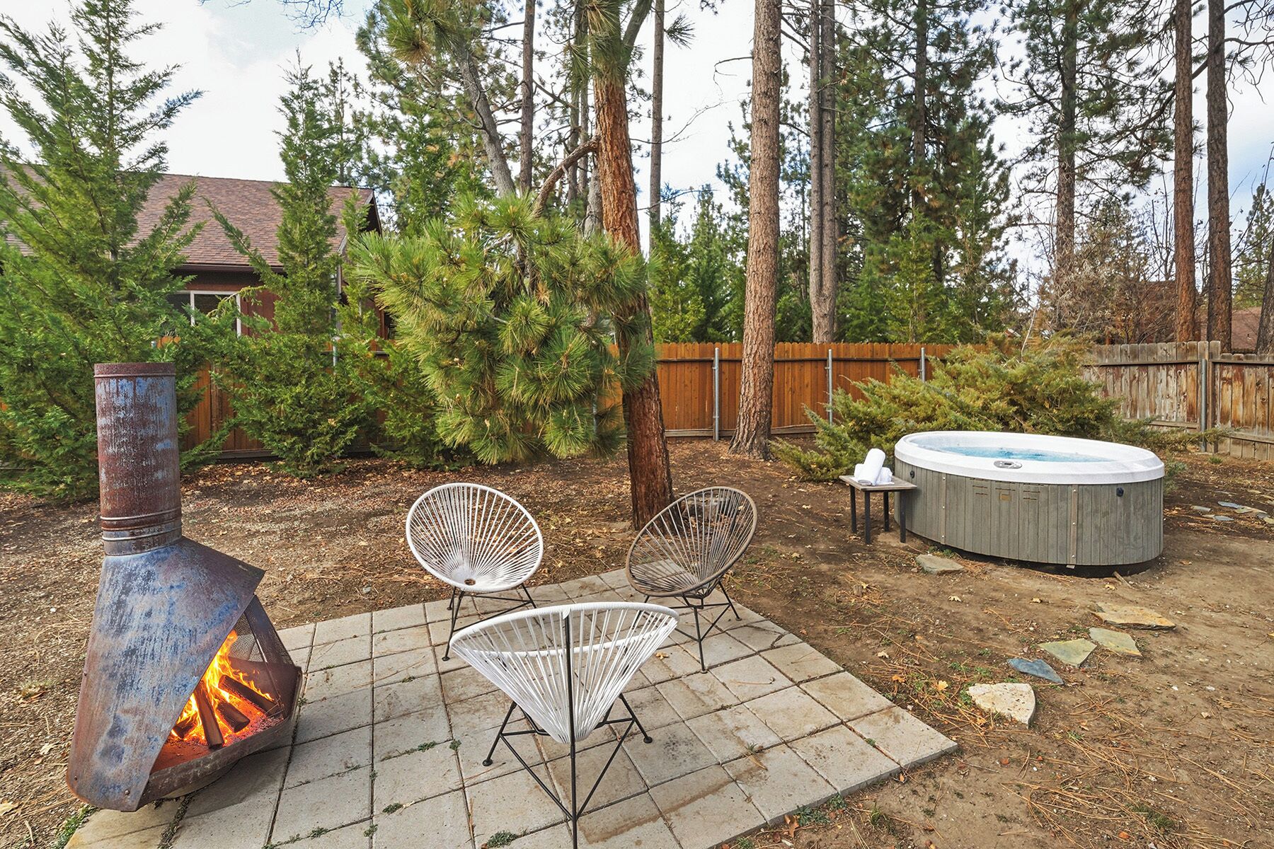 Un patio al aire libre con un brasero de metal, dos sillas blancas de metal y un jacuzzi.