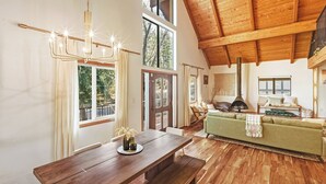 A spacious living area with a wooden ceiling, a dining table, a green sofa, and a fireplace. - Close to Ski Slopes & Trails ~ Zoo ~ Hot Tub (Big Bear)