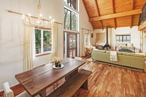 Ein geräumiger Wohnbereich mit Holzboden, einem Esstisch, einem grünen Sofa und einem Kamin.
