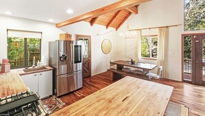 A modern kitchen with a large wooden table, stainless steel appliances, and a view of greenery outside. - Close to Ski Slopes & Trails ~ Zoo ~ Hot Tub (Big Bear)