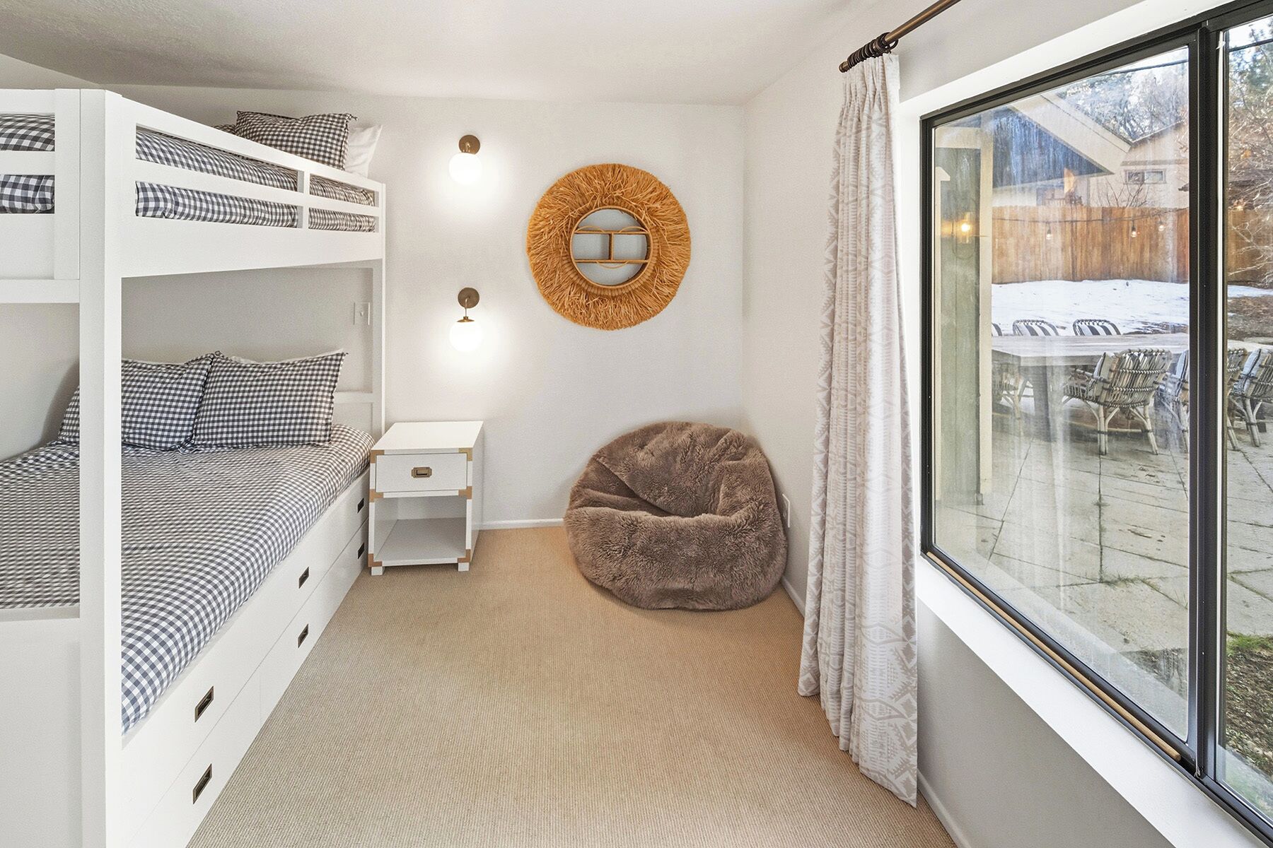 Een slaapkamer met stapelbedden, een nachtkastje, een ronde spiegel, een relax fauteuil en een groot raam met uitzicht.