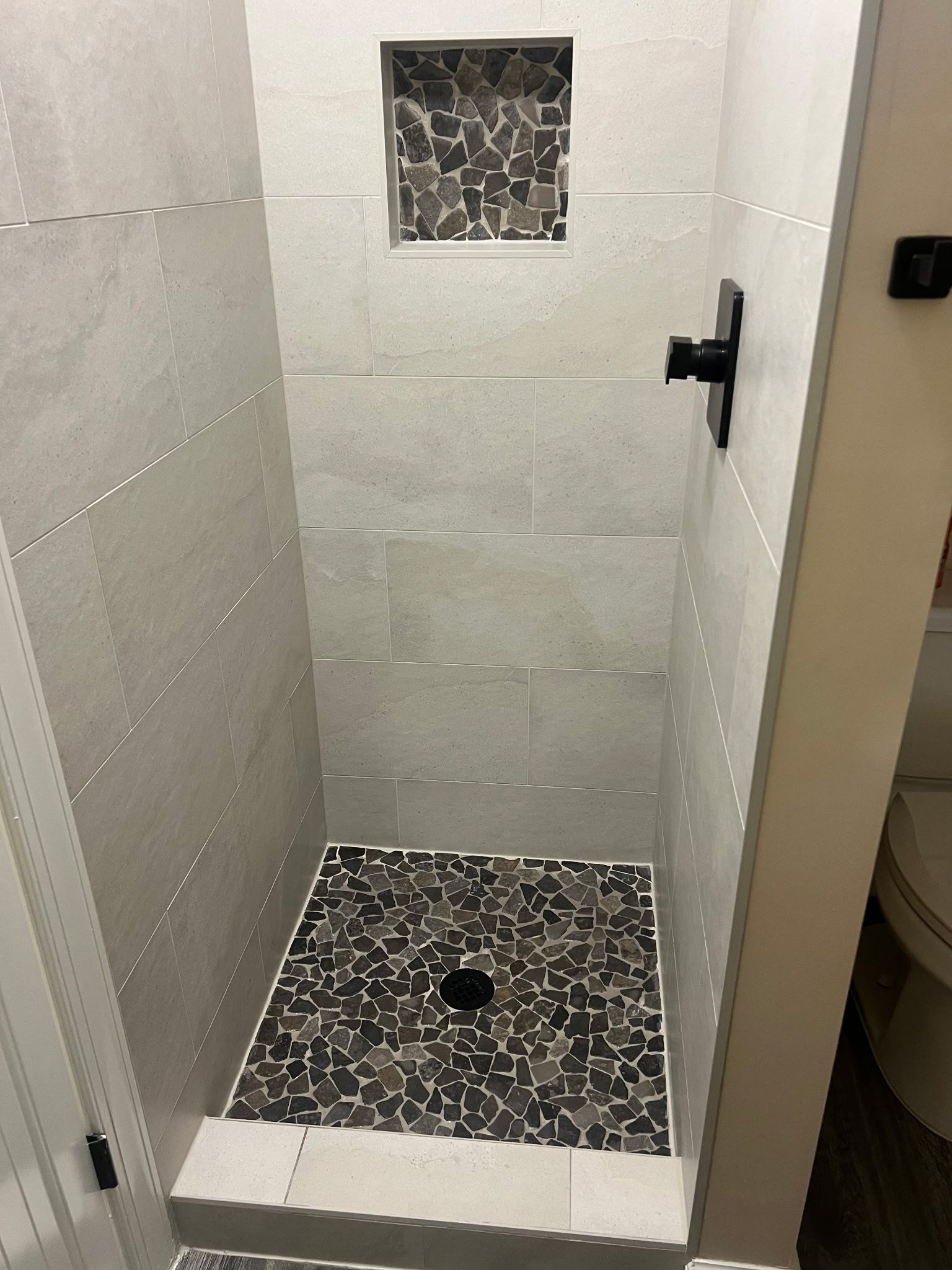A shower with a stone mosaic floor and a small stone accent wall.