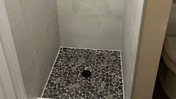 A shower with a stone mosaic floor and a small stone accent wall.