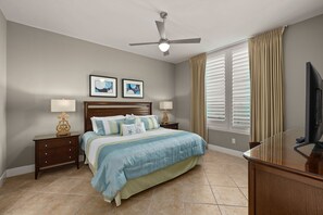 A bedroom with a bed, two bedside tables, a ceiling fan, a TV, and a window with curtains. - Sapphire #1403 | Luxury Beachfront Resort • 14th Floor Gulf Views • Pool (South Padre Island)
