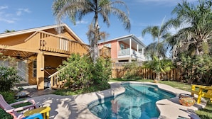 Un jardin avec une piscine, une terrasse en bois et un espace clos agrémenté de palmiers.