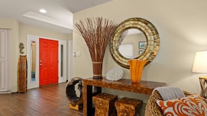 Un intérieur moderne avec un plancher en bois, une porte rouge, un miroir décoratif et un vase contenant de longues branches.
