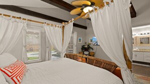 Une chambre à coucher avec un lit à baldaquin, un ventilateur de plafond et une salle de bain équipée d’un meuble-lavabo et d’un miroir.