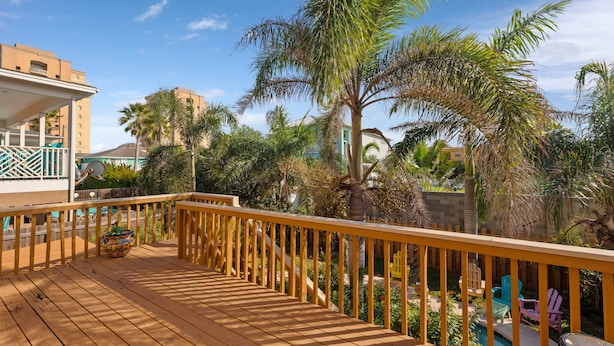 Une terrasse en bois dotée d’une rambarde, qui offre une vue sur une piscine et une végétation luxuriante.
