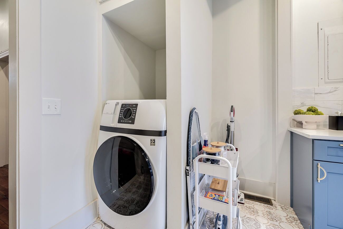 A compact laundry area with a washing machine, a drying rack, and a small kitchen area with a sink and countertop.