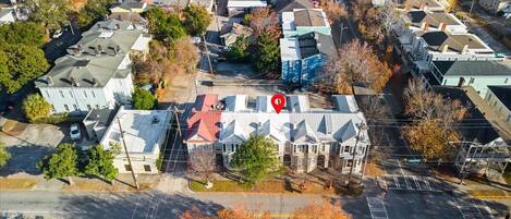 An aerial view of a residential area with houses, streets, and a prominent building with a red marker on its roof.