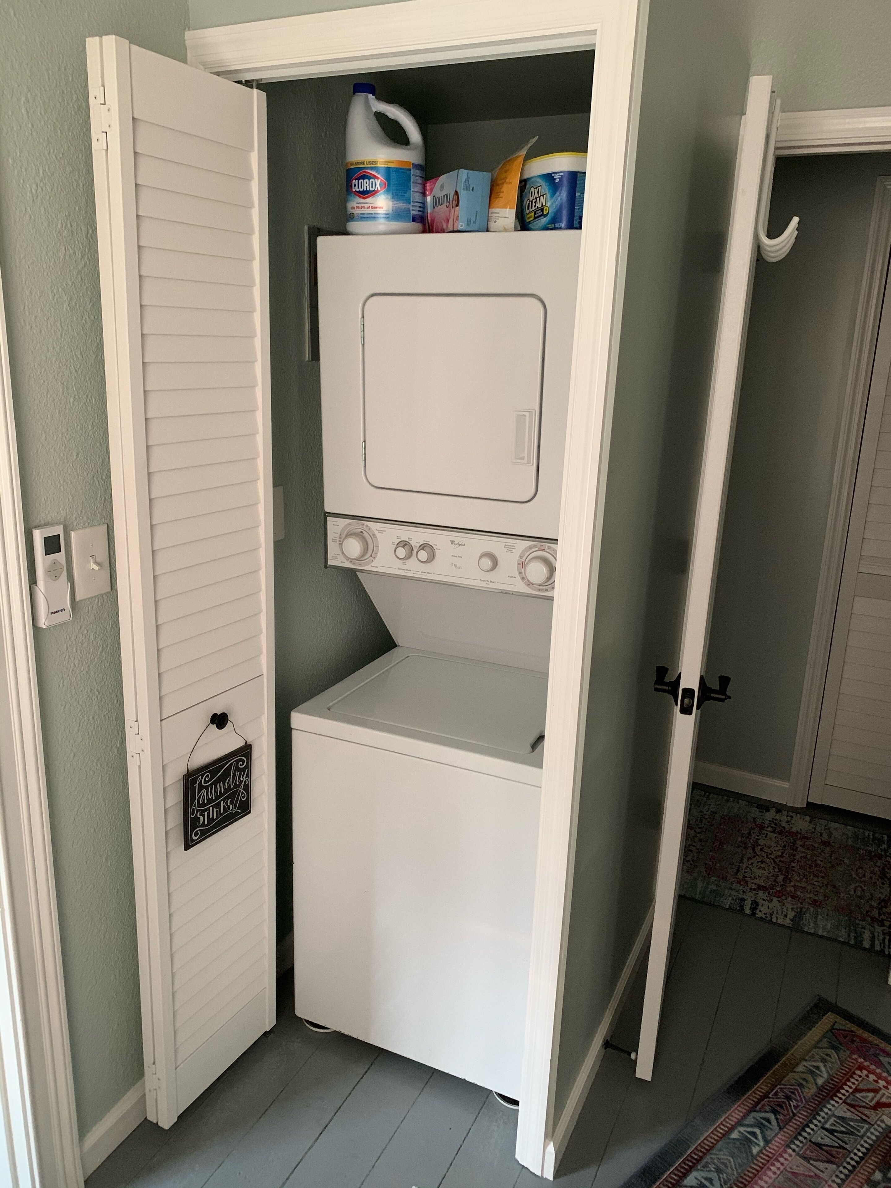 A laundry room with a front-loading washer and dryer, a small shelf with cleaning supplies, and a door with a laundry sign.
