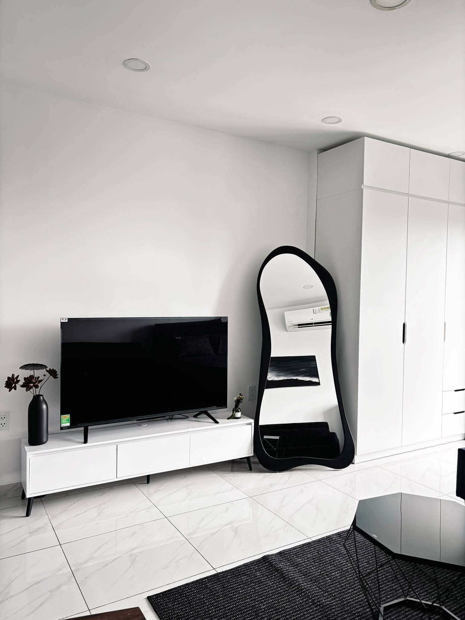 Een moderne woonkamer met een flatscreen televisie, een grote spiegel en een wit kastje.
