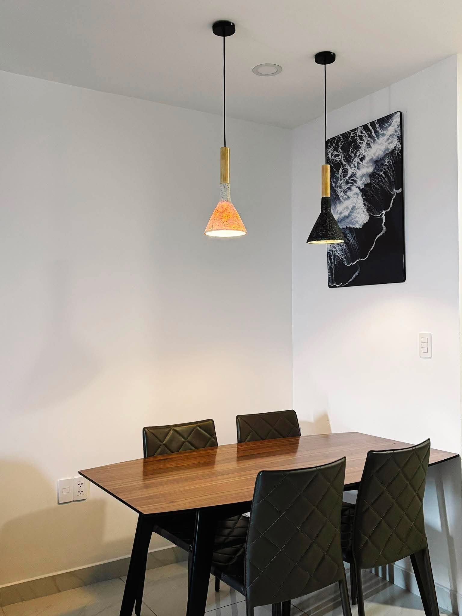 A dining area with a wooden table and four chairs, two pendant lights, and a wall-mounted artwork.