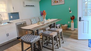Een keuken met een blauwgroene accentmuur, witte kasten, een houten eettafel met barstoelen en een hangend kunstwerk.