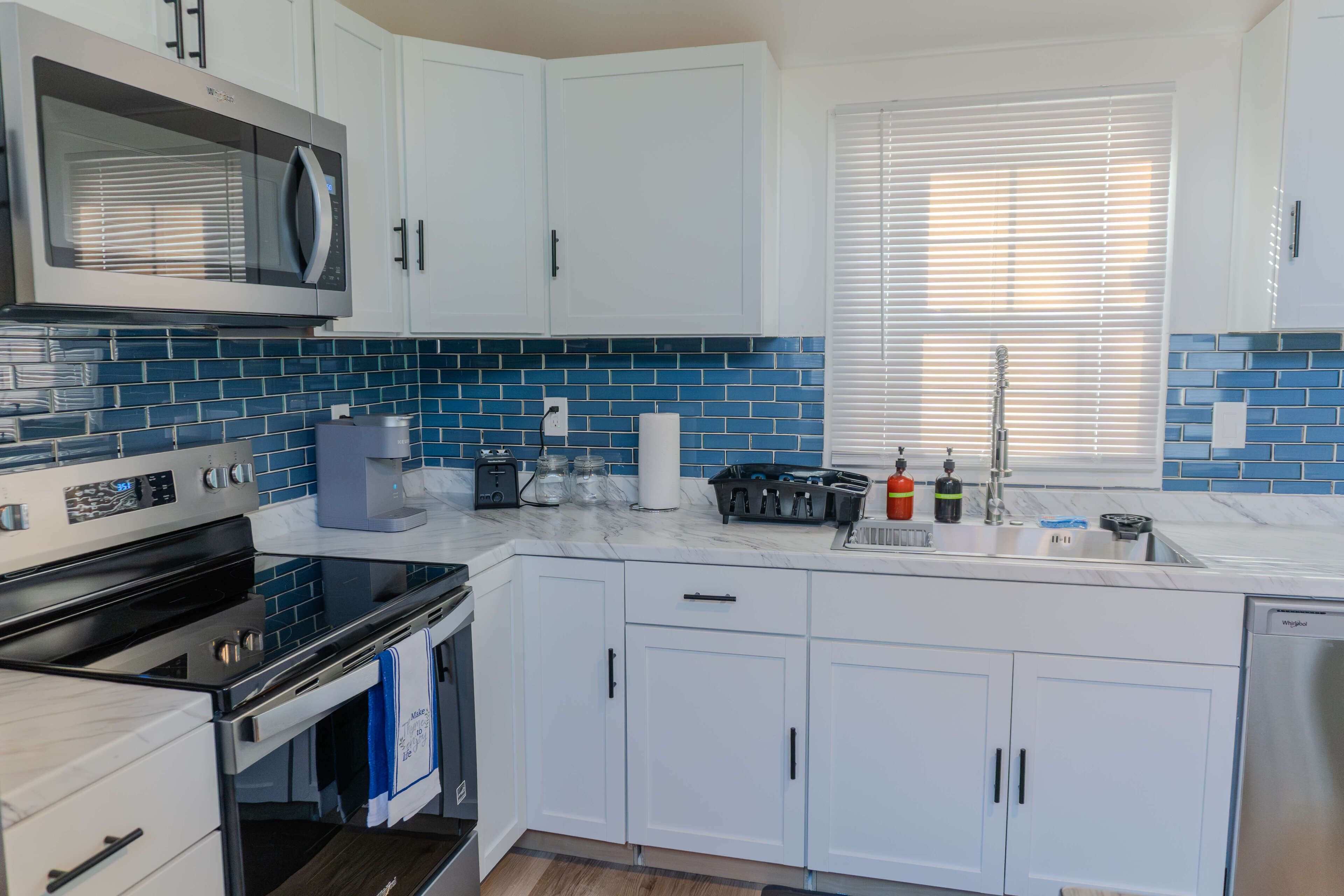 Et moderne køkken med hvide skabe, en stålfarvet mikrobølgeovn og en backsplash i blå fliser.