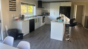 A modern kitchen with white cabinets, a central island, and a bar area with stools. - Far North holiday base with panoramic coastline outlook and comfy sleepout (Kaitaia)