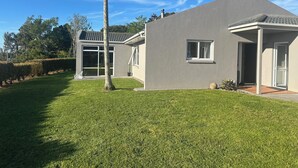 A modern house with a well-maintained lawn, a large window, and a door. - Far North holiday base with panoramic coastline outlook and comfy sleepout (Kaitaia)