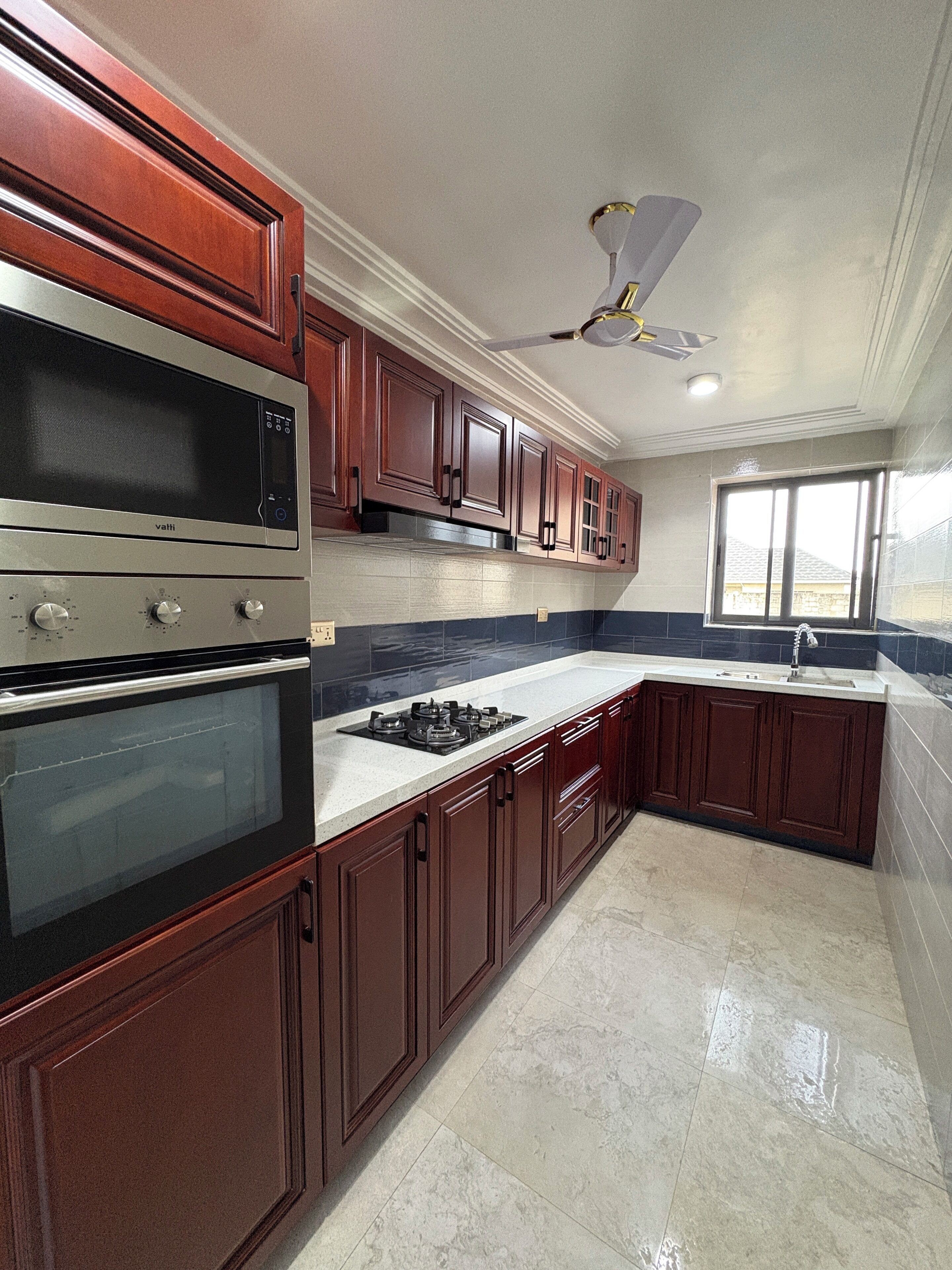 Una cocina moderna con armarios de madera oscura, electrodomésticos de acero inoxidable y un amplio ventanal que aporta luz natural.