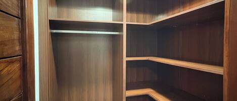 A corner closet with wooden shelves and drawers, a ceiling light, and a tiled floor.