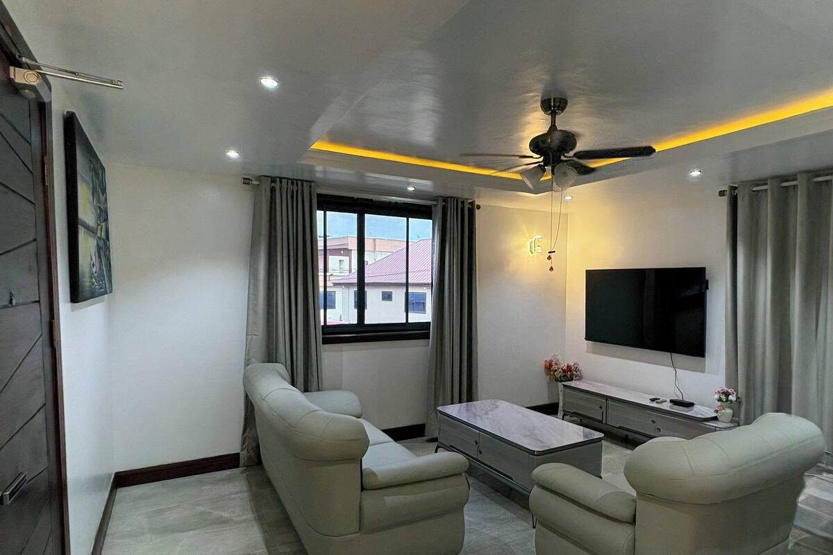A modern living room with two sofas, a TV, a ceiling fan, and a window with curtains.