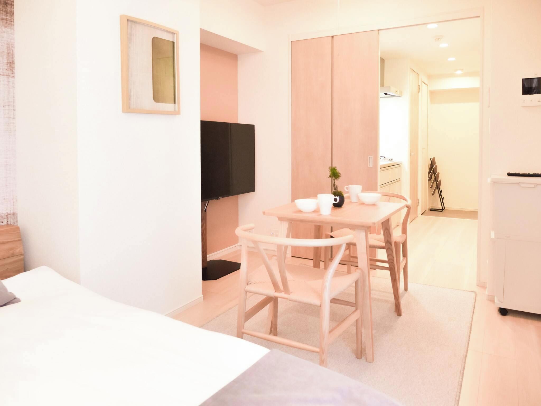 Une chambre d’hôtel moderne équipée d’un lit, d’un bureau avec des chaises, d’une télévision et d’une petite table avec des tasses et une plante.