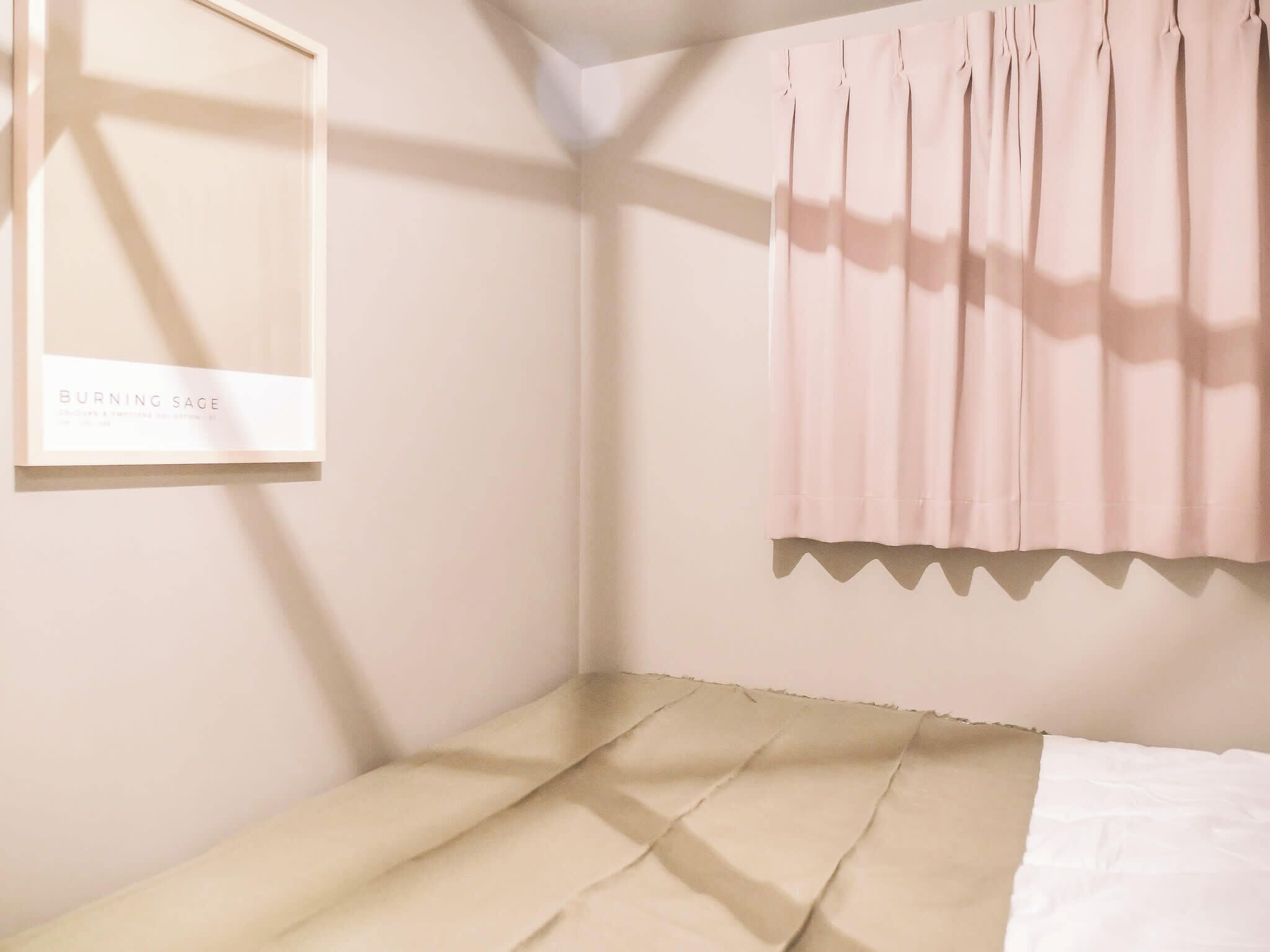 Una habitación minimalista con una cama, un cuadro en la pared y una ventana con cortinas.