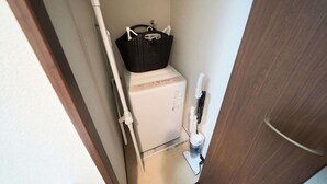 Un bagno piccolo con un water bianco, un cesto nero appoggiato sul water, un asciugamani elettrico bianco e una spazzola bianca per la pulizia.