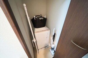 A compact bathroom with a white toilet, a black basket on the back of the toilet, a white hand dryer, and a white cleaning brush. - Asakusa Kototoibashi Facing Tokyo Skytree (Sumida City)