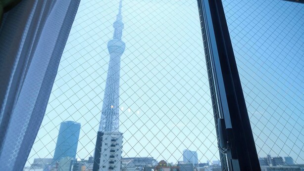 Vista attraverso una finestra con zanzariera, che mostra un'alta torre e gli edifici circostanti.