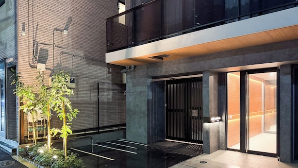 En moderne bygning med murstensfacade, en lågeindgang og et lille udendørs område med beplantning.