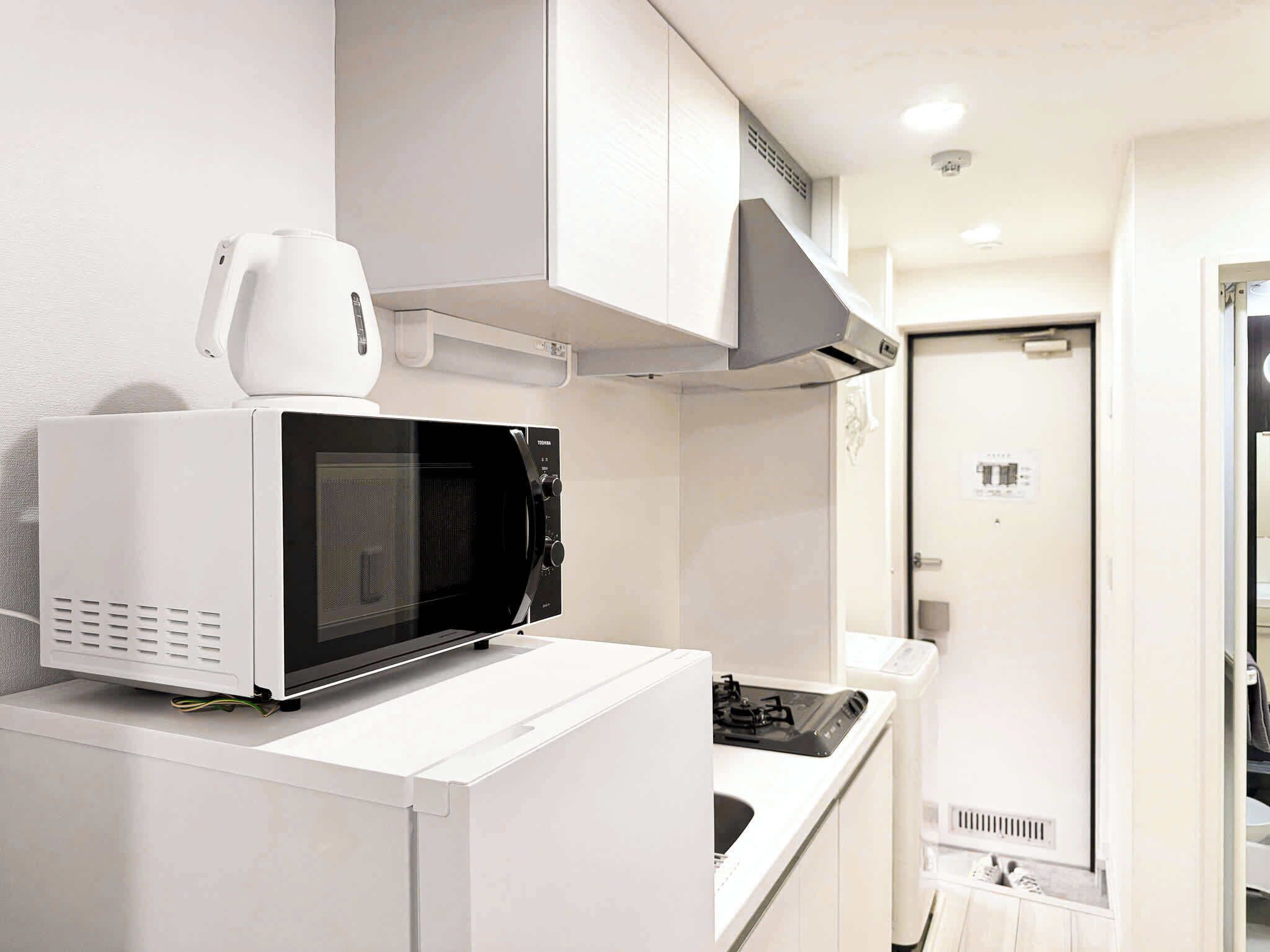 A compact kitchenette with a microwave, a small stove, and a white cabinet.