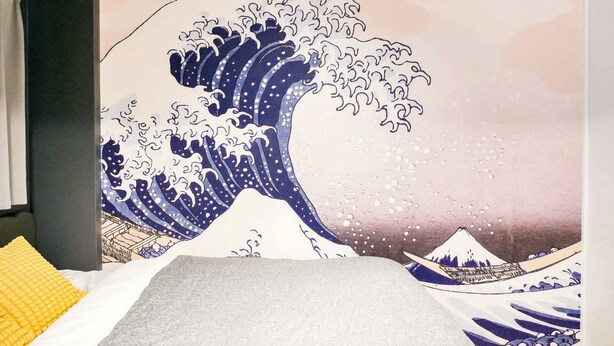 A room with a large wave painting on the wall, a bed with a grey blanket, and a yellow pillow. - Triphome Asakusa Alpha 3min to Sensoji Temple (Taito City)